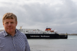 Tim stands near the water with a CalMac ferry in the background